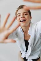 joven mujer adolescente escuchando a música con estéril auriculares y bailando hogar, sonriendo con dientes con un corto Corte de pelo en un blanco camisa en un blanco antecedentes. niña natural poses con No filtros foto