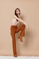 woman in brown pants and bra raised her leg up on beige background photo