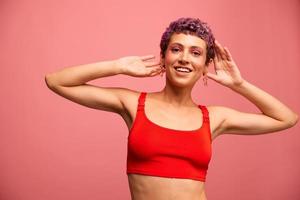 Fashion portrait of a woman with a short haircut of purple color and a smile with teeth in a red top on a pink background happiness photo