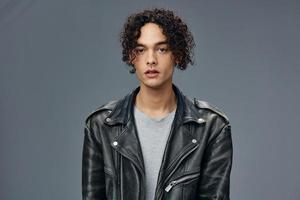 Pretty sexy self-confident stylish tanned curly man leather jacket posing isolated on over gray studio background. Cool fashion offer. Huge Seasonal Sale New Collection concept. Copy space for ad photo