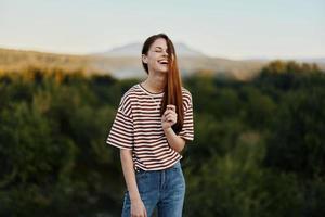 A young woman laughs and looks at the camera in simple clothes against the backdrop of a beautiful landscape of mountains and trees in autumn photo