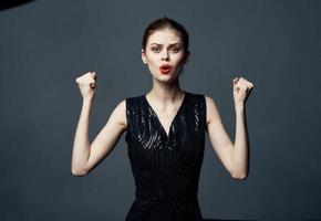 Elegant lady in a black dress on a gray background gestures with her hands emotions surprise joy photo