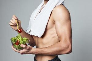 sporty man with a towel on his shoulders plate of salad inflated torso gray background close-up photo