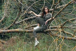 woman in overalls and sneakers sits on a tree branch model photo