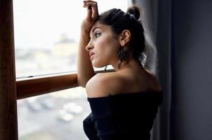 bonito mujer en un negro vestir cerca el ventana posando elegante estilo foto