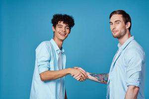 curly guy in a shirt stands next to a young man in a t-shirt on a blue background cropped view photo