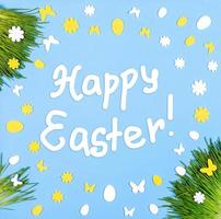 Happy Easter card with frame of green grass, decorative white and yellow eggs and flowers on blue. photo