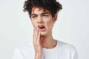 guy in white t-shirt with curly hair pain in the teeth health problems photo