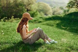 Top view A young female freelance student in a yellow cap, top, and green pants is working on her cell phone sitting on the green grass in the park. Lifestyle and concept of a young healthy society photo