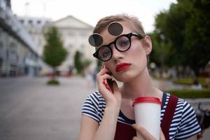 mujer con corto pelo en el calle vistiendo lentes vaso con bebida caminar foto