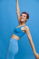 joven atlético Moda mujer con de colores pelo y corto Corte de pelo posando y bailando en azul ropa de deporte sonriente y mirando a el cámara en un azul monocromo antecedentes foto