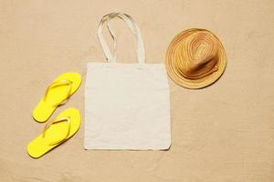 Mockup shopper handbag beach sand background. Top view copy space shopping eco reusable bag. Flip flops accessories. Template blank top view white cotton material canvas cloth. Empty mock-up beach photo