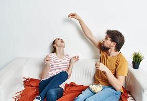 un hombre y un mujer en un brillante habitación sentar en el sofá con palomitas de maiz en un plato emociones amigos verde flor en un maceta foto