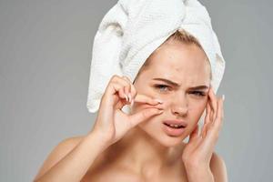 pretty woman with towel on her head squeezes out pimples on her face photo