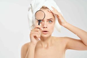 surprised woman with bare shoulders clean skin magnifying glass in hands health problems photo