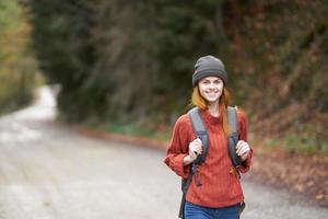 woman with a backpack in full growth walks along the road in the forest in autumn photo