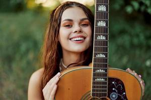 Young hippie woman with eco image smiling and looking into the camera with guitar in hand in nature on a trip photo