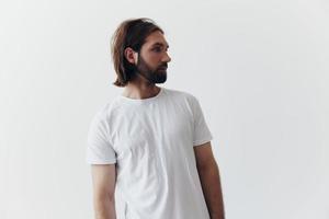 Portrait of a man with a black thick beard and long hair in a white T-shirt on a white isolated background emotion of sadness and longing photo