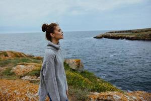pretty woman in a gray sweater stands on a rocky shore nature Relaxation concept photo