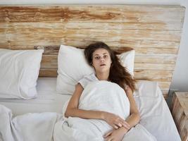 a woman with a surprised expression lies in bed in the morning under the covers photo