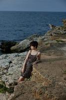 woman in a shiny dress stands on the stone coast of the ocean nature unaltered photo