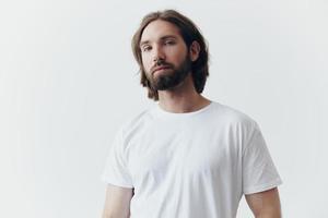 Portrait of a man with a black thick beard and long hair in a white T-shirt on a white isolated background emotion of sadness and longing photo