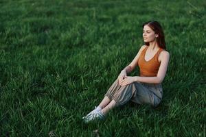 A happy woman looks out at the setting summer sun sitting on the fresh green grass in the park and smiling, view from above. The concept of self-care photo