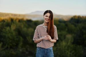 A young woman laughs and looks at the camera in simple clothes against the backdrop of a beautiful landscape of mountains and trees in autumn photo