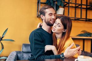 young people in love hugging while sitting at a table in a cafe and orange wall interior photo