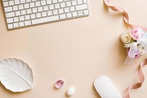 Office Desk workspace-a flat layout of the workspace layout with roses, decorative stones and a computer on a beige pastel background. The desktop background concept photo