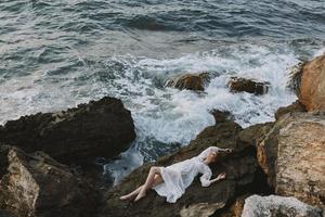 woman in long white dress wet hair lying on a rocky cliff unaltered photo