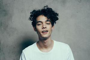 Cheerful guy with curly hair tilts his head to the side on a gray background photostudio model photo