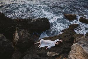 Beautiful bride in long white dress wet hair lying on a rocky cliff unaltered photo