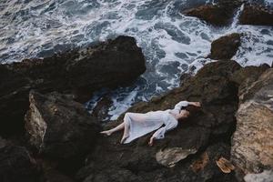 beautiful young woman lying on her back on a rocky seashore unaltered photo