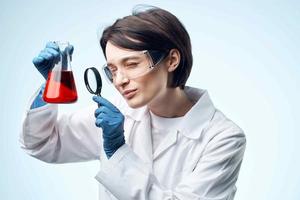 mujer científico mirando mediante un aumentador vaso a un químico solución trabajo biotecnología foto