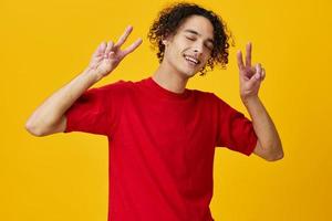 linda gracioso caucásico joven hombre en rojo camiseta espectáculo signo v gesto posando aislado en terminado amarillo estudio antecedentes. el mejor oferta con gratis sitio para publicidad. emociones para todos los días concepto foto