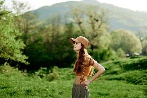 A beautiful woman in sportswear and a cap walks against a green natural landscape and smiles in the sunlight photo