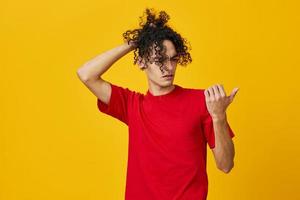 Funny pensive Caucasian young man in red t-shirt point finger at free place posing isolated on yellow studio background. The best offer with free place for advertising. Emotions for everyday concept photo