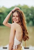 A young woman smiling in an image of a hippie and eco-dress dancing in nature by the lake wearing a hat and yellow pants in the summer sunset photo