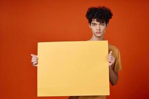 guy with curly hair yellow poster in hands studio advertising photo