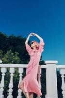 glamorous woman pink dress modern style stands near the railing sunny day photo