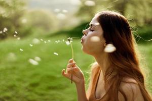 un hembra persona de libre dedicación paseos despreocupado y felizmente en un verde parque y golpes apagado un diente de león flor en el puesta de sol ligero foto