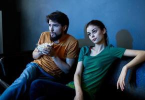 emotional woman and man with a plate of popcorn watching tv in the evening indoors photo