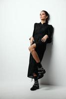 pretty woman in black dress leaning against the wall light background photo