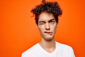 cute guy in white t-shirt curly hair grimace orange background photo