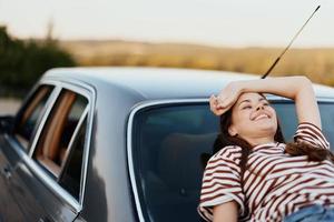 The woman driver stopped on the road and lay down on the car to rest and look at the beautiful landscape in a striped T-shirt and jeans. Complicated journey to nature photo