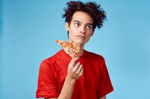 man holding a slice of pizza in his hand and curly hair red t-shirt blue background photo