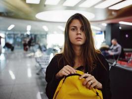 mujer sentado a el aeropuerto amarillo mochila esperando para un vuelo foto