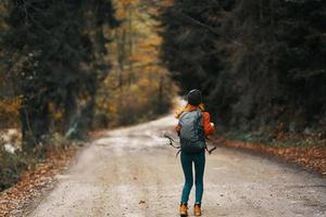 happy woman hiker with backpack walks on the road in autumn forest photo
