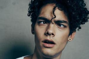 portrait of a handsome guy with curly hair on a gray background white t-shirt close-up model photo